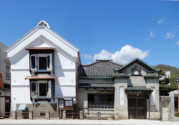 写真：白い壁に黒い屋根のレトロな雰囲気の建物.写真左に店蔵、右側に白磁タイルが貼られた事務所