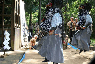写真：獅子舞の頭部を被った和装の男性たちが社の前で踊っている様子