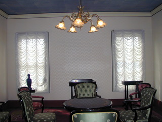 写真：ビロード張りの椅子やシャンデリア、窓にレースカーテンの付いた上品な部屋