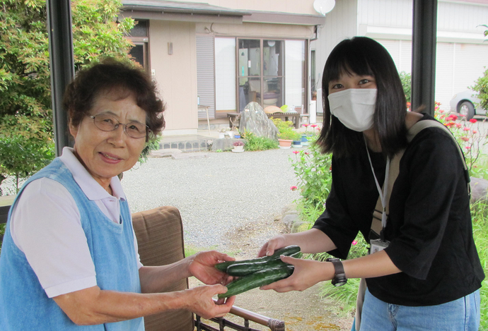 高齢者に自分で栽培したきゅうりを渡す小島隊員の写真