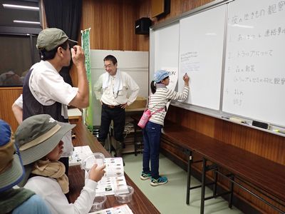 写真:屋内で図鑑をひろげ、調べた種名をホワイトボードに書いていく、大人より子どもたちが熱心