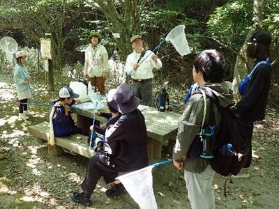 写真:虫取り網をもつ講師を囲んで話を聞く親子