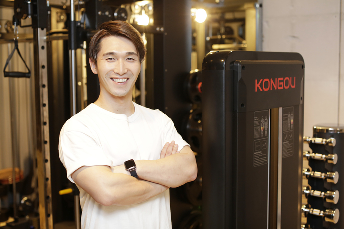 写真：トレーニング器具の前で腕を組む江原さん