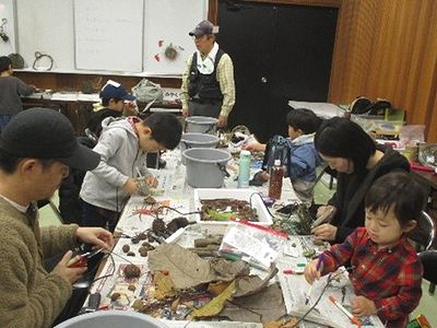 写真:テーブルの上にたくさんの落ち葉や木の実を載せて作品作りに没頭する親子
