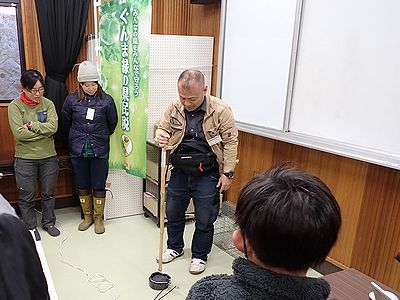写真:動物の脚に見立てた棒を罠に差し込もうとする講師と緊張した様子で見守る参加者
