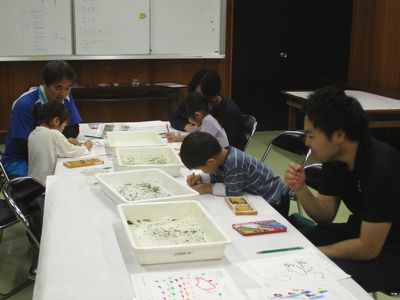 写真:バッドの中のオタマジャクシなどのを覗き込みながら絵を描く
