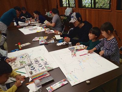 写真：机に大きいマップを広げて、図鑑を見ながら真剣に取り組む親子