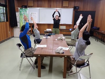 写真:椅子に座ったまま、腕を上げて背筋を伸ばす参加者