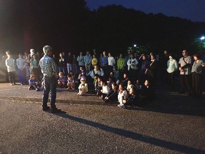 写真：駐車場で講師を囲みホタルのお話を聞く参加者たち