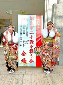 写真:二十歳を祝う会の看板の前で撮影 女性2人